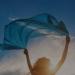 a woman flies a blue scarf over her head with the sky in the background a woman flies a blue scarf over her head with the sky in the background
