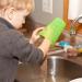 Boy washing a green cup in the kitchen sink