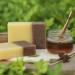 Bars of brown and yellow coloured soap with jar of honey in a garden