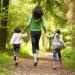 A woman hold hands with two children, skipping through the woods.