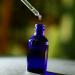a glass dropper dispensing liquid over a blue glass bottle a glass dropper dispensing liquid over a blue glass bottle