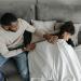 A father of African descent comforts his daughter who is sick in bed.